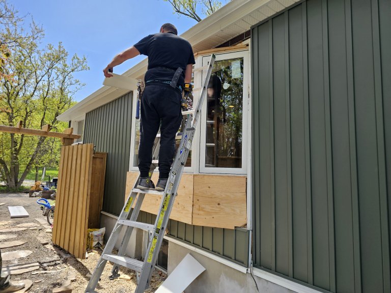 Installer working from a ladder during exterior window replacement, showing why outside access should be kept clear.